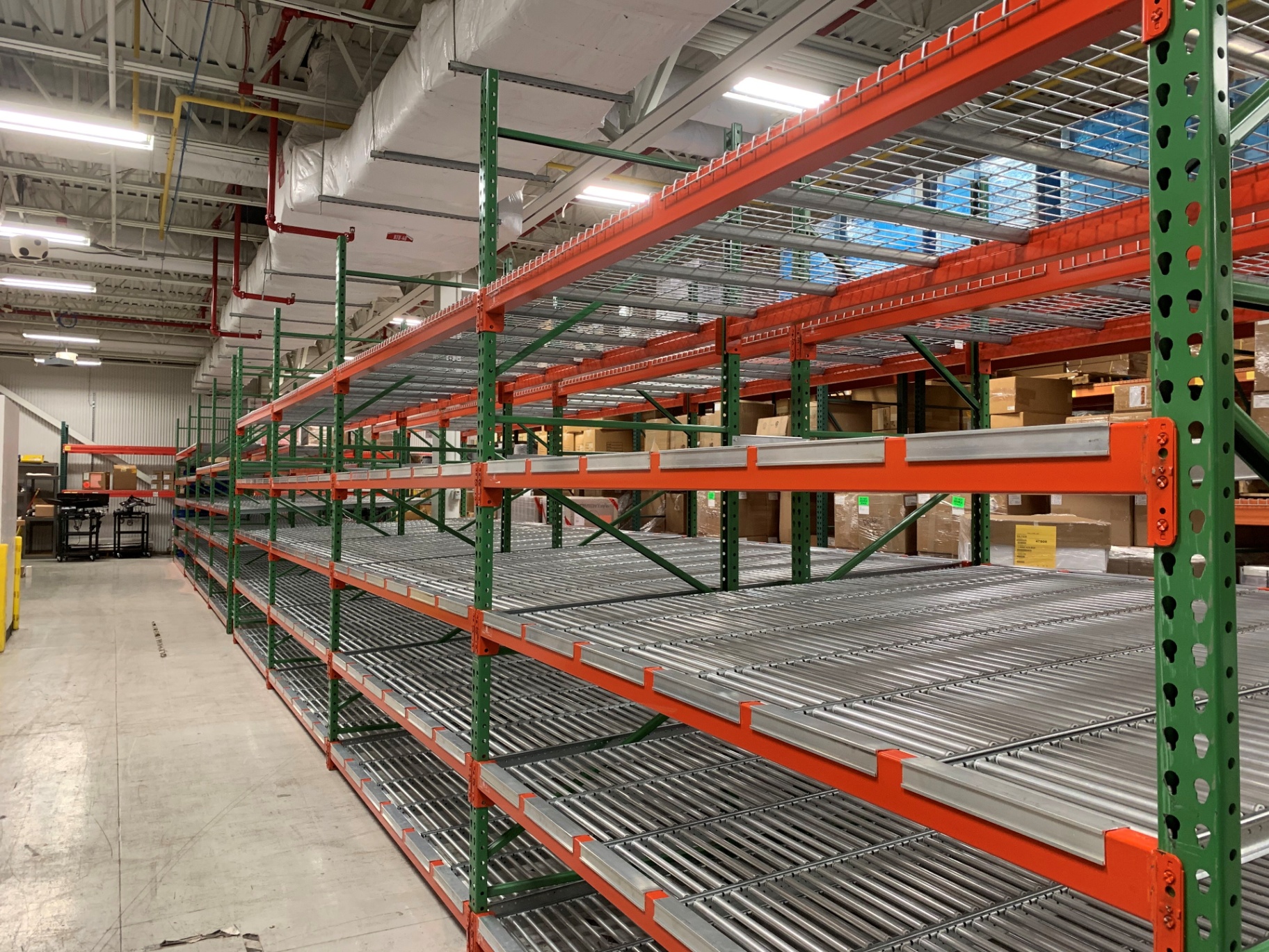 Carton flow racking with green uprights, orange beams, and roller lanes