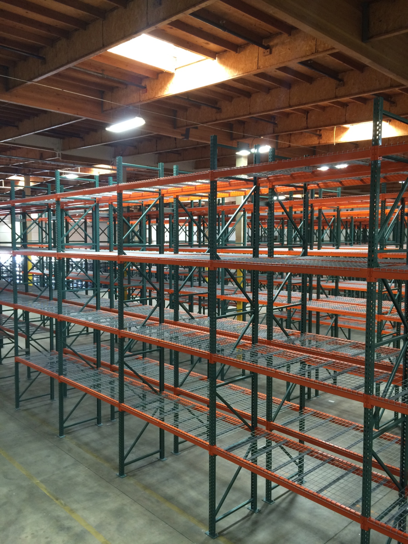 Multi-level selective pallet racking with green uprights, orange beams, and wire decking